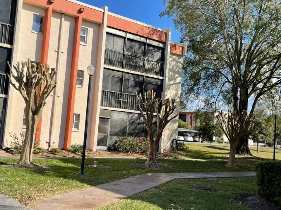 Apartment building with peach and gray фасade, leafless trees, and a sidewalk in a grassy courtyard