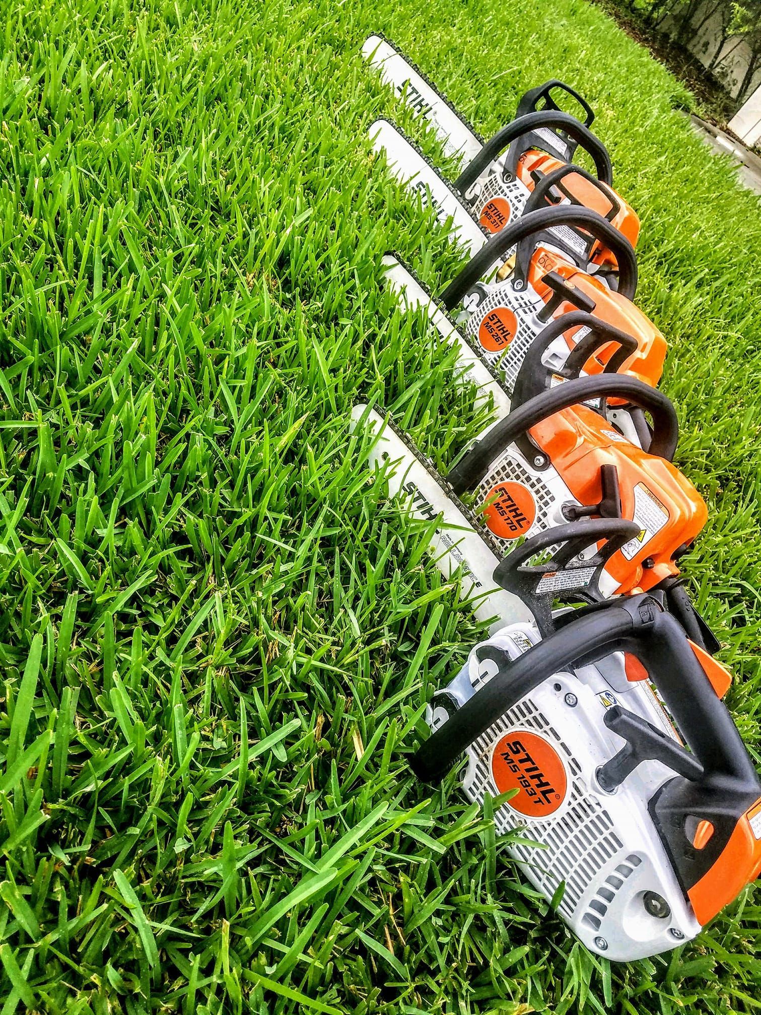 Several orange-and-white hedge trimmers lined up on green grass outdoors