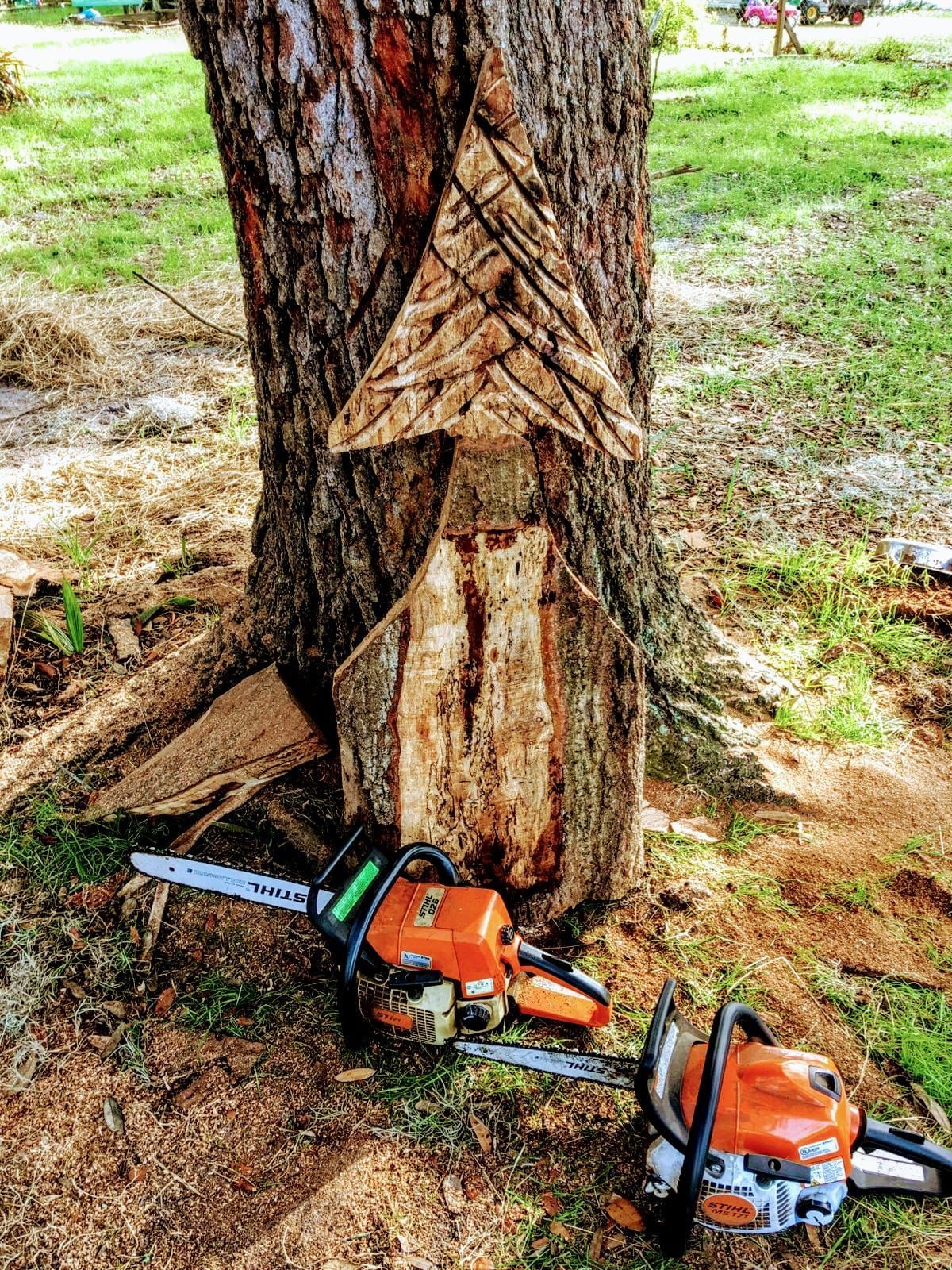 Two orange chainsaws at the base of a tree with cut marks in a grassy yard