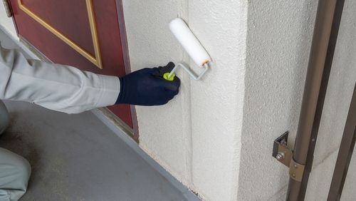 A gloved hand with a paint roller painting a white wall dark grey