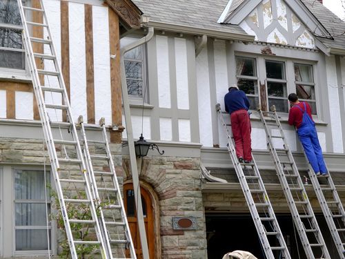 Two men on ladders painting the outside of a two-story house
