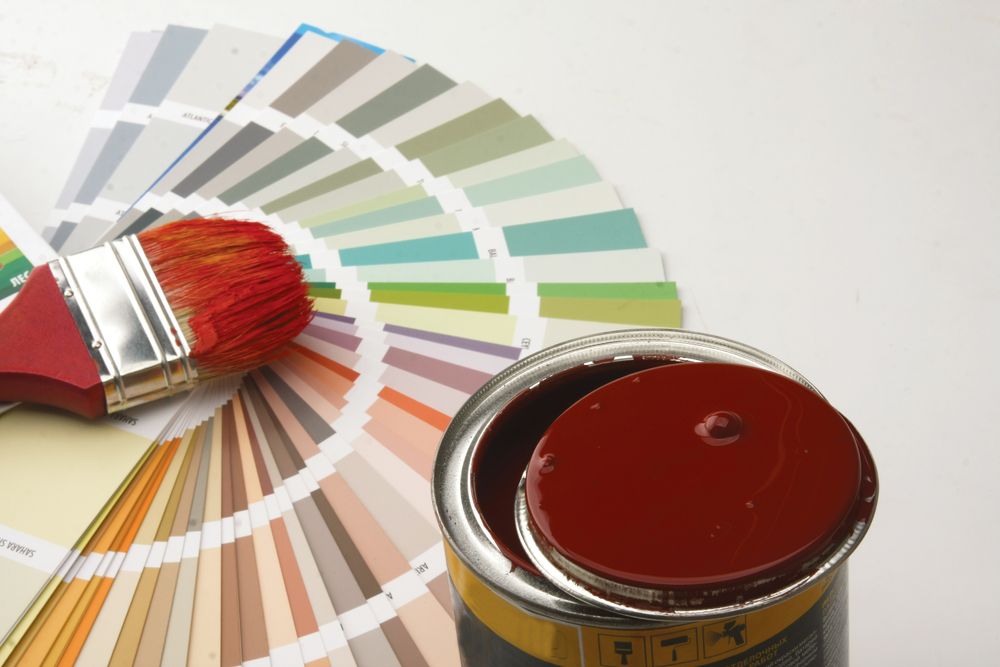A fan of paint samples with a paint brush sitting on top, with an open can of dark red paint next to it
