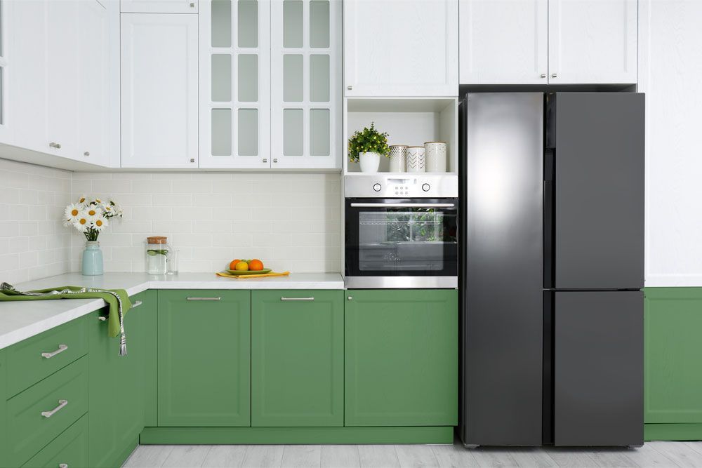 A kitchen with white and green cabinets next to a black fridge