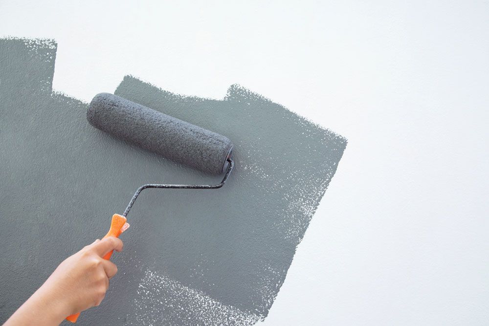 A hand with a paint roller painting a white surface dark grey