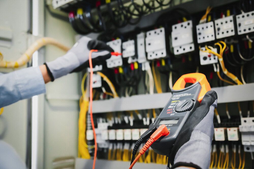 An Electrician is Using a Clamp Meter to Test an Electrical Panel — Sigley Electrical in Mooball, NSW