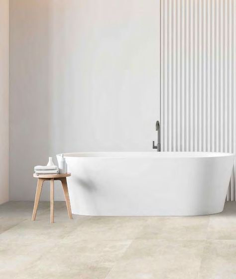 Una vasca da bagno bianca freestanding è addossata a una parete rivestita con pannelli a doghe verticali, accanto a un piccolo tavolino in legno.