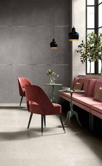 Interni moderni di un bar con sedie e panche in velluto rosa, tavoli rotondi e pareti piastrellate grigio scuro.