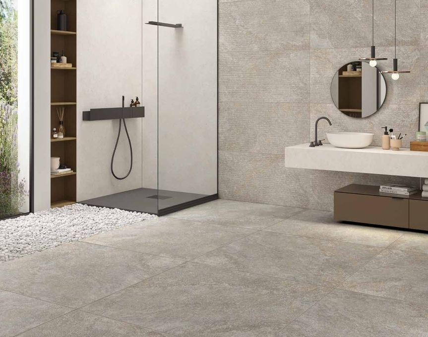 Bagno moderno con cabina doccia in vetro, pareti con finitura effetto pietra, mobile lavabo sospeso e specchio rotondo.