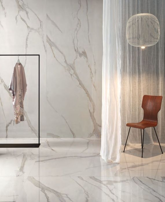 Una stanza con pavimento e pareti in marmo bianco, uno stand appendiabiti sulla sinistra, una tenda bianca trasparente e una poltrona in pelle.