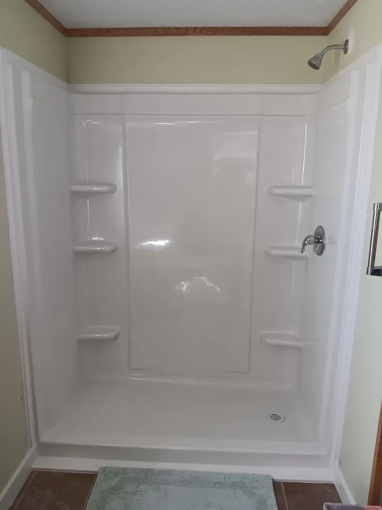 A white, multi-piece shower stall with built-in shelving, a chrome shower head, and a faucet, set against tan walls.