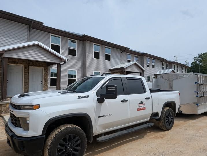 White pickup truck parked beside a gray apartment building, towing a large enclosed trailer.