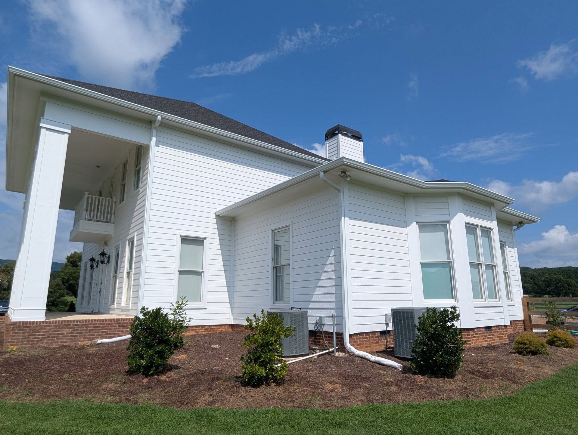 Modern white house with large porch, pitched roof, and landscaped front yard under a blue sky