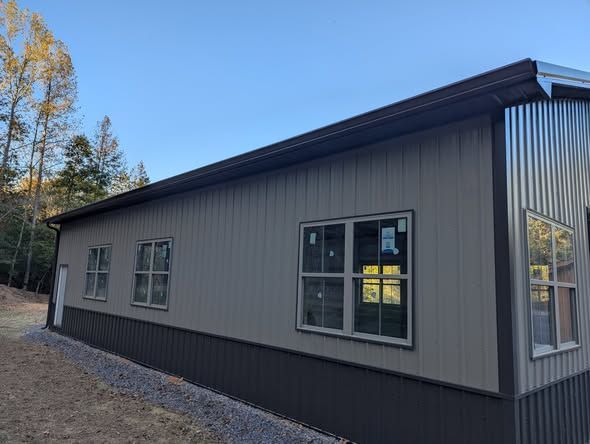 Exterior of a gray metal building with dark trim and windows on a wooded lot