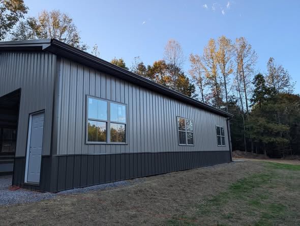 Modern gray metal building with windows and a white door beside a grassy yard and trees