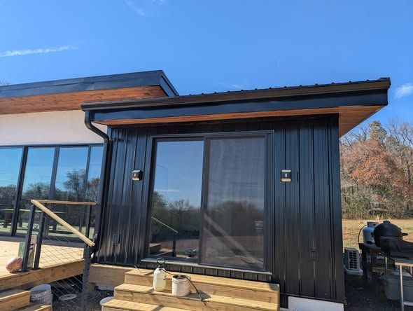Modern black cabin exterior with large glass door and windows, under blue sky