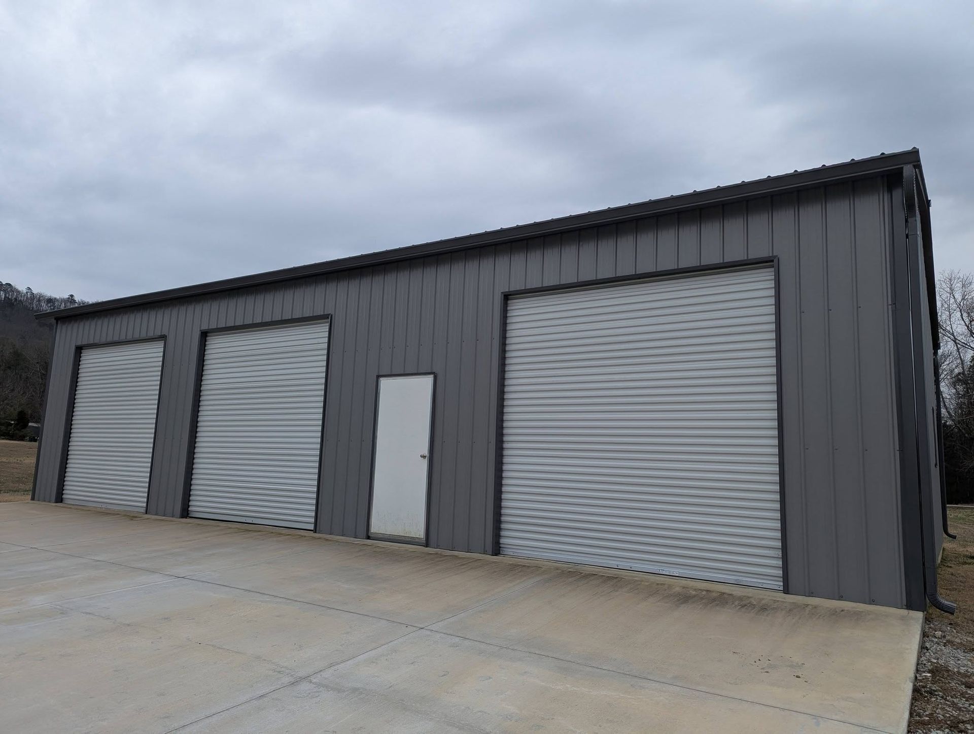 Gray metal storage building with several roll-up doors and a small side door on a concrete lot