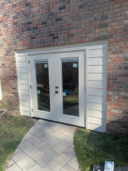 White double French doors set in a brick wall, opening onto a small paved patio.