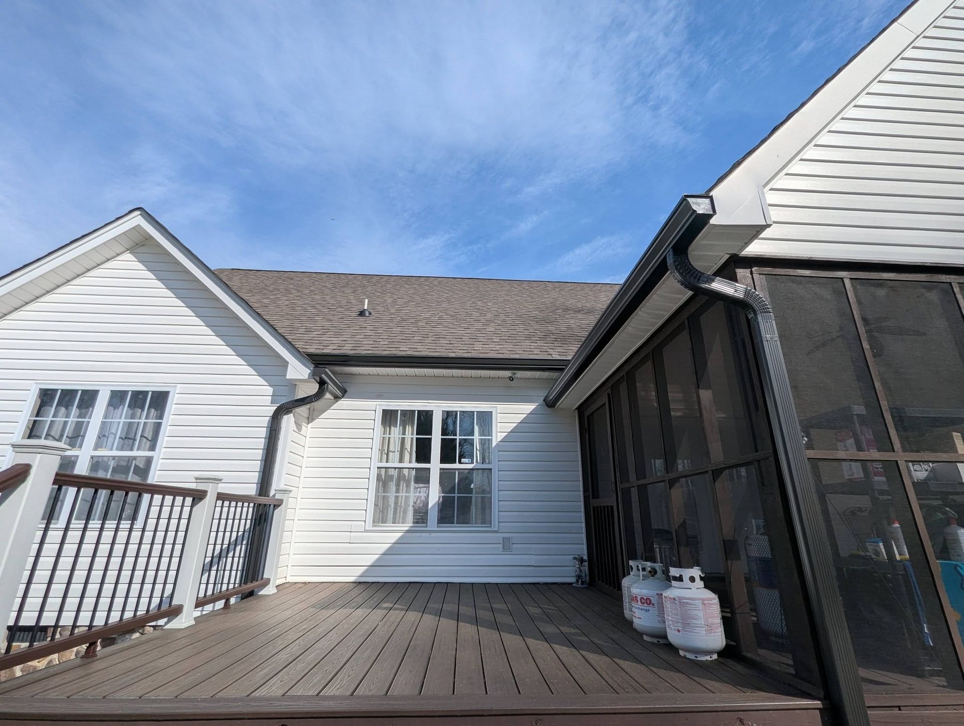 Back porch with white siding, wooden deck, screened area, and propane tanks under a blue sky