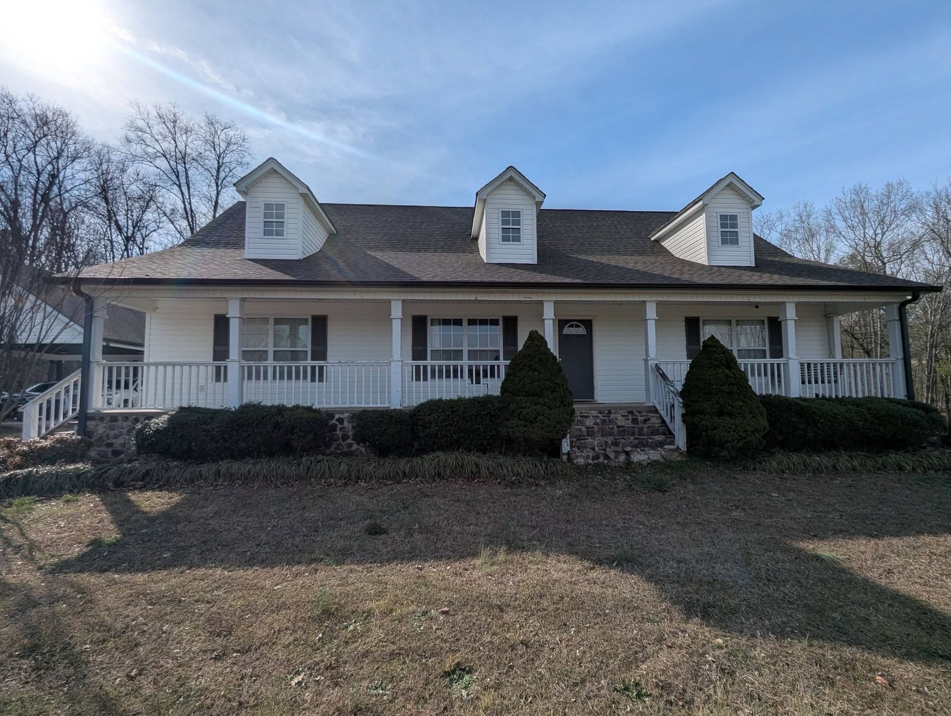 White farmhouse with porch and three dormer windows, set in a yard under a clear sky.