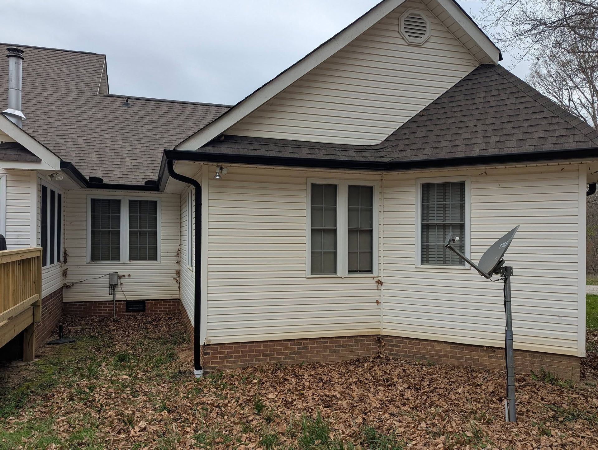 Back of a beige house with white trim, leaf-covered yard, and a satellite dish on a post