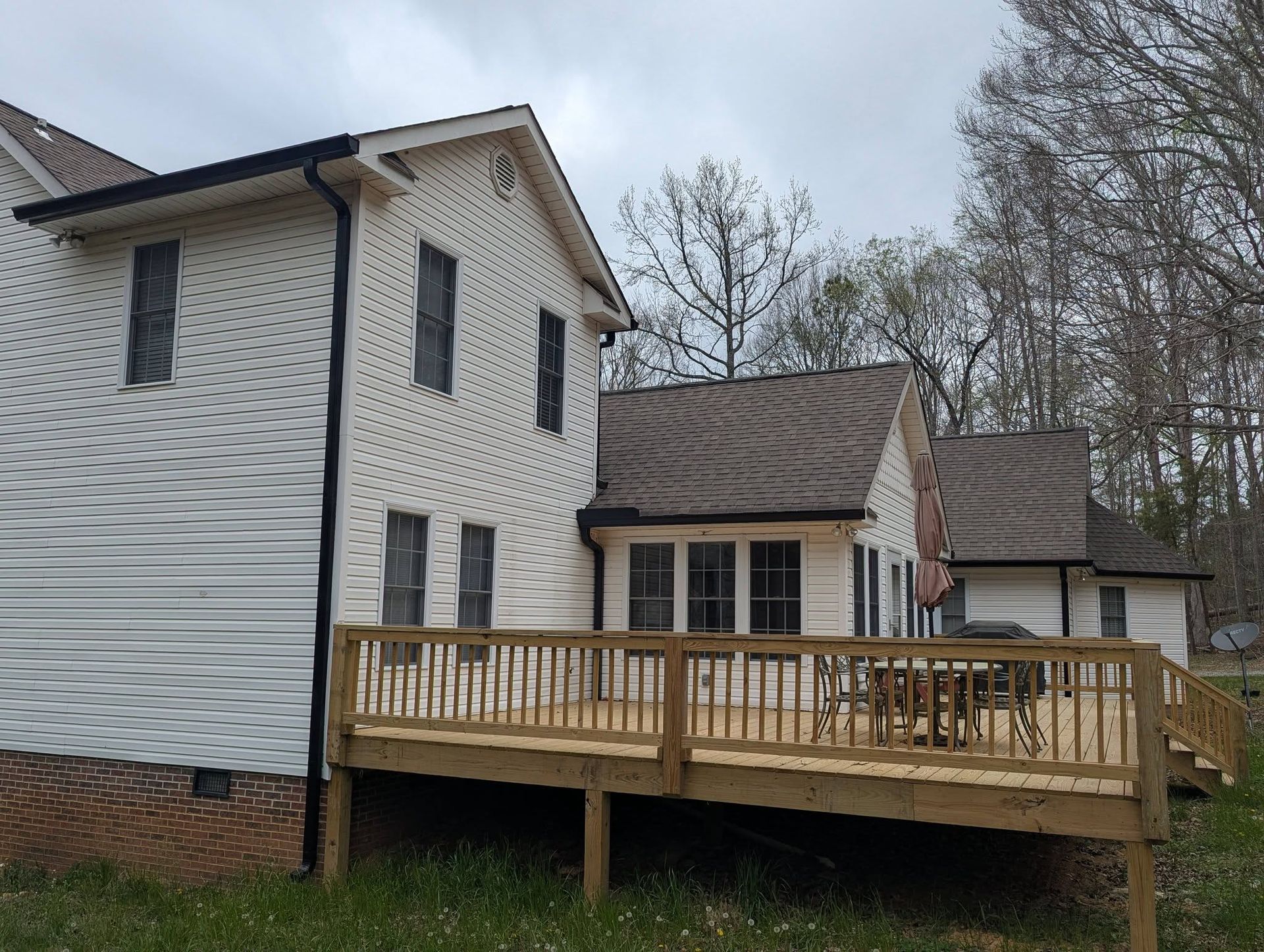 Two-story white house with a wooden deck and patio furniture in a wooded yard
