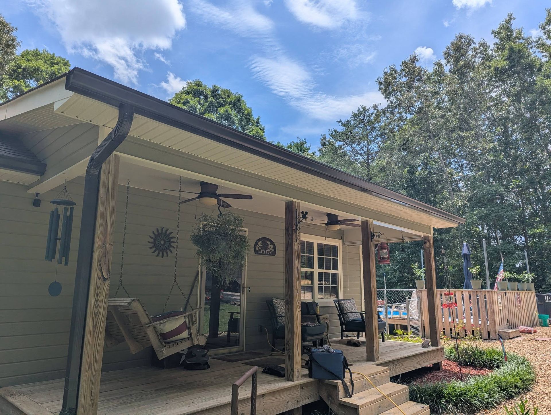 Covered front porch with a swing, hanging plants, and a landscaped yard under a blue sky.