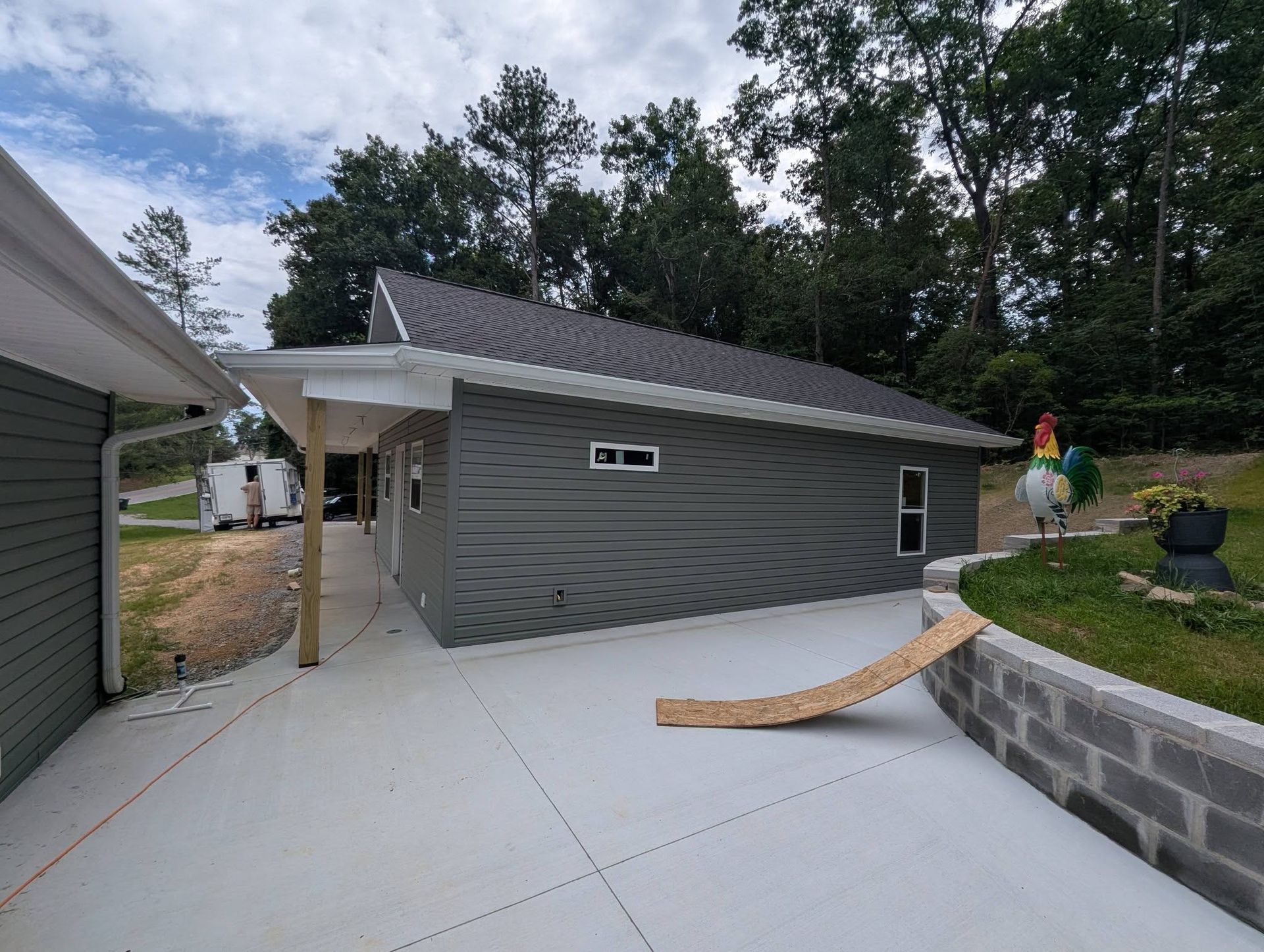 Gray house exterior with a new concrete patio, curved paver wall, and a worker on the right side.
