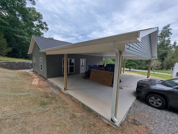 Carport attached to a house with a black SUV parked beside it and a wooded yard in the background