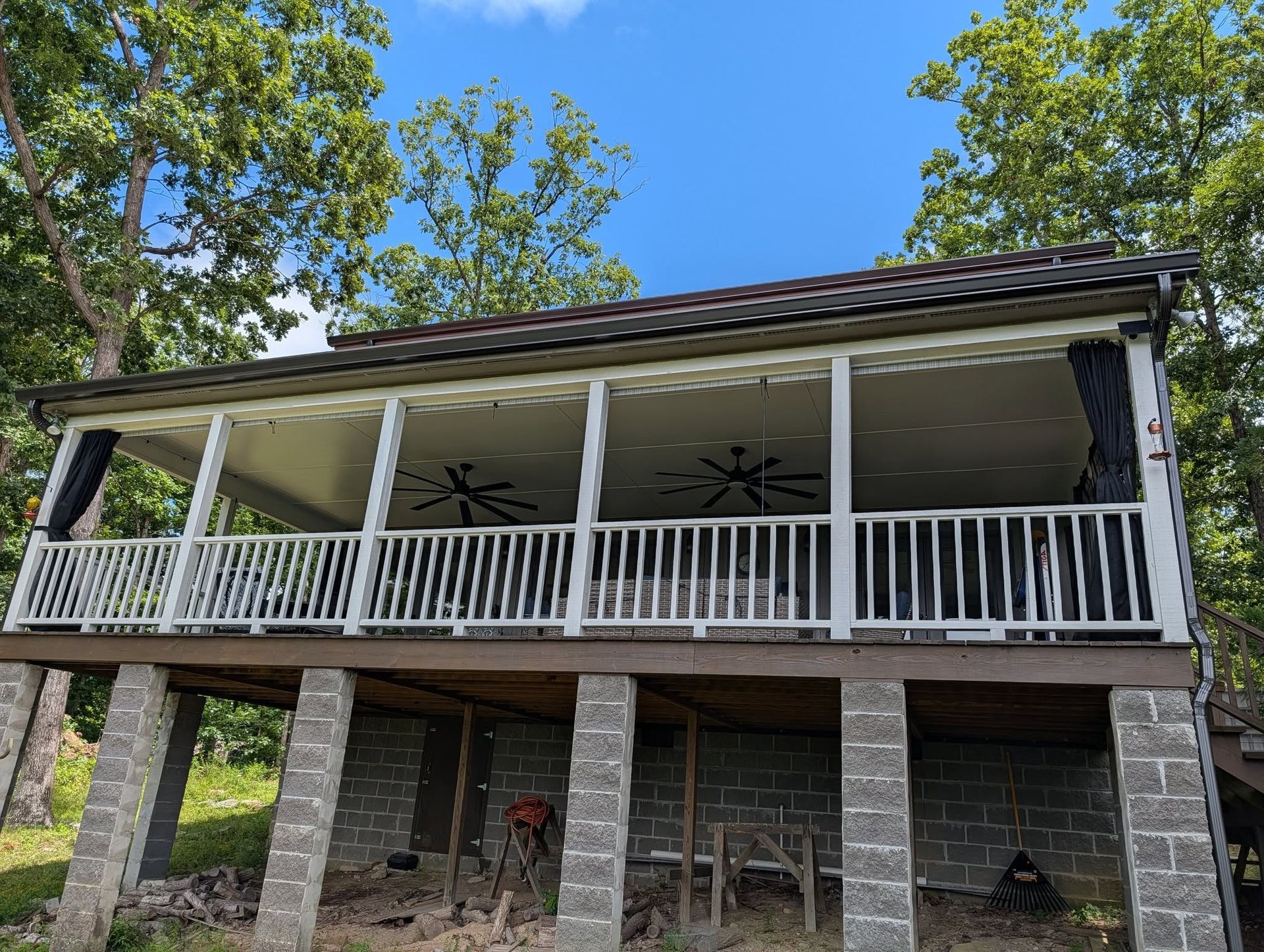 Stone house with a raised porch, white railing, and dark roof under a blue sky