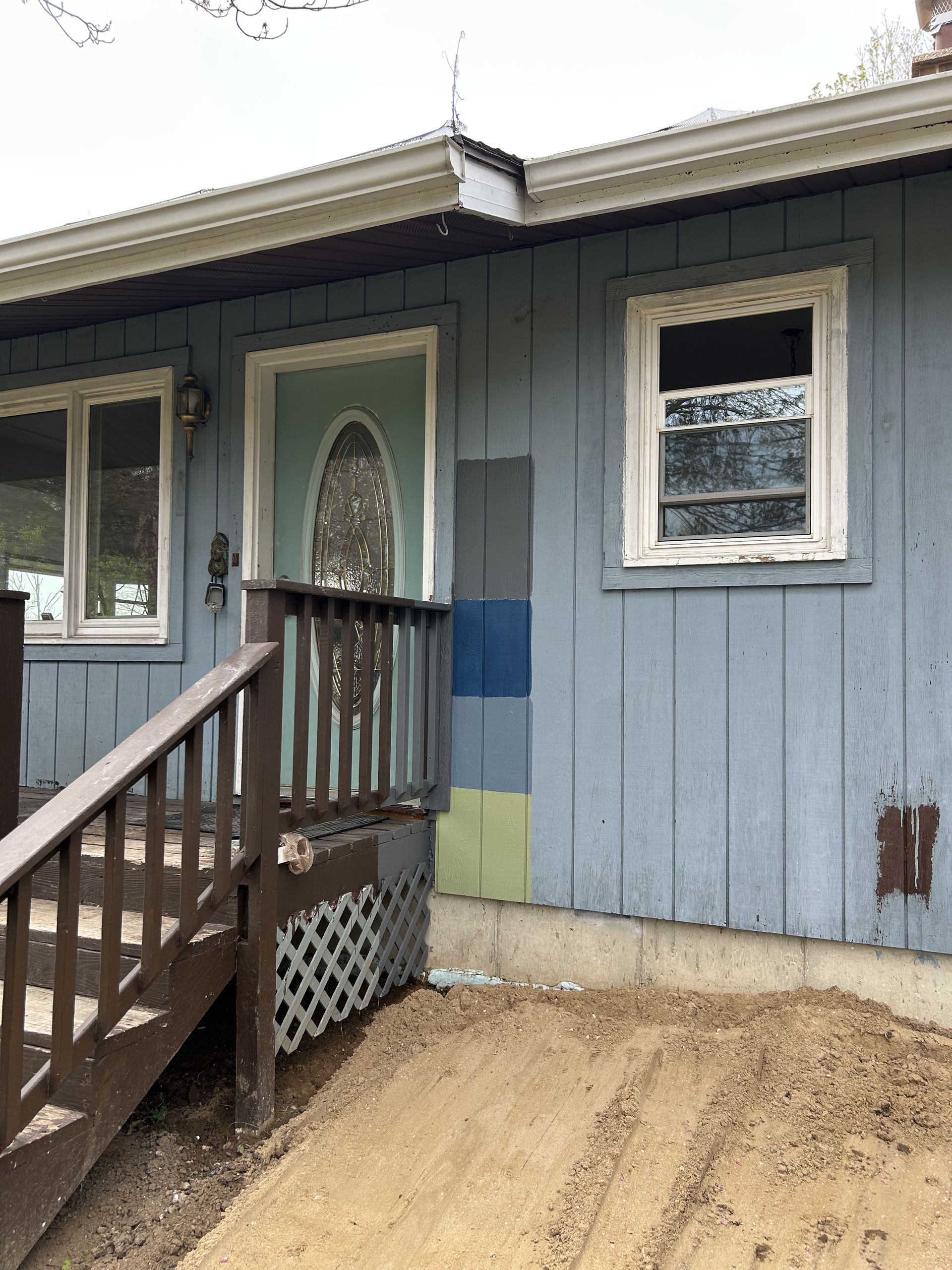 Blue-gray house exterior with a small wooden porch, steps, and white-trimmed windows
