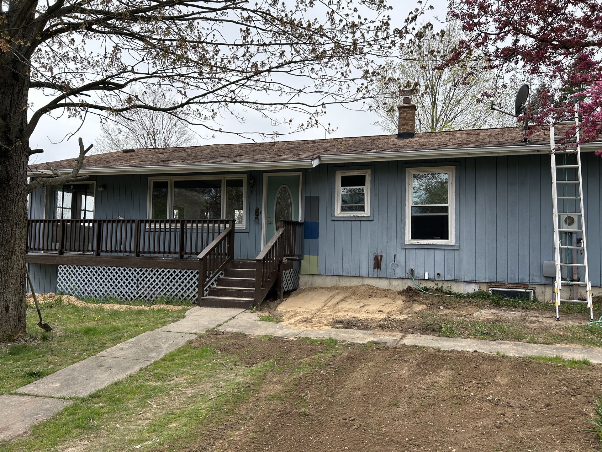 Single-story blue house with a front porch, steps, and a ladder leaning against the right side