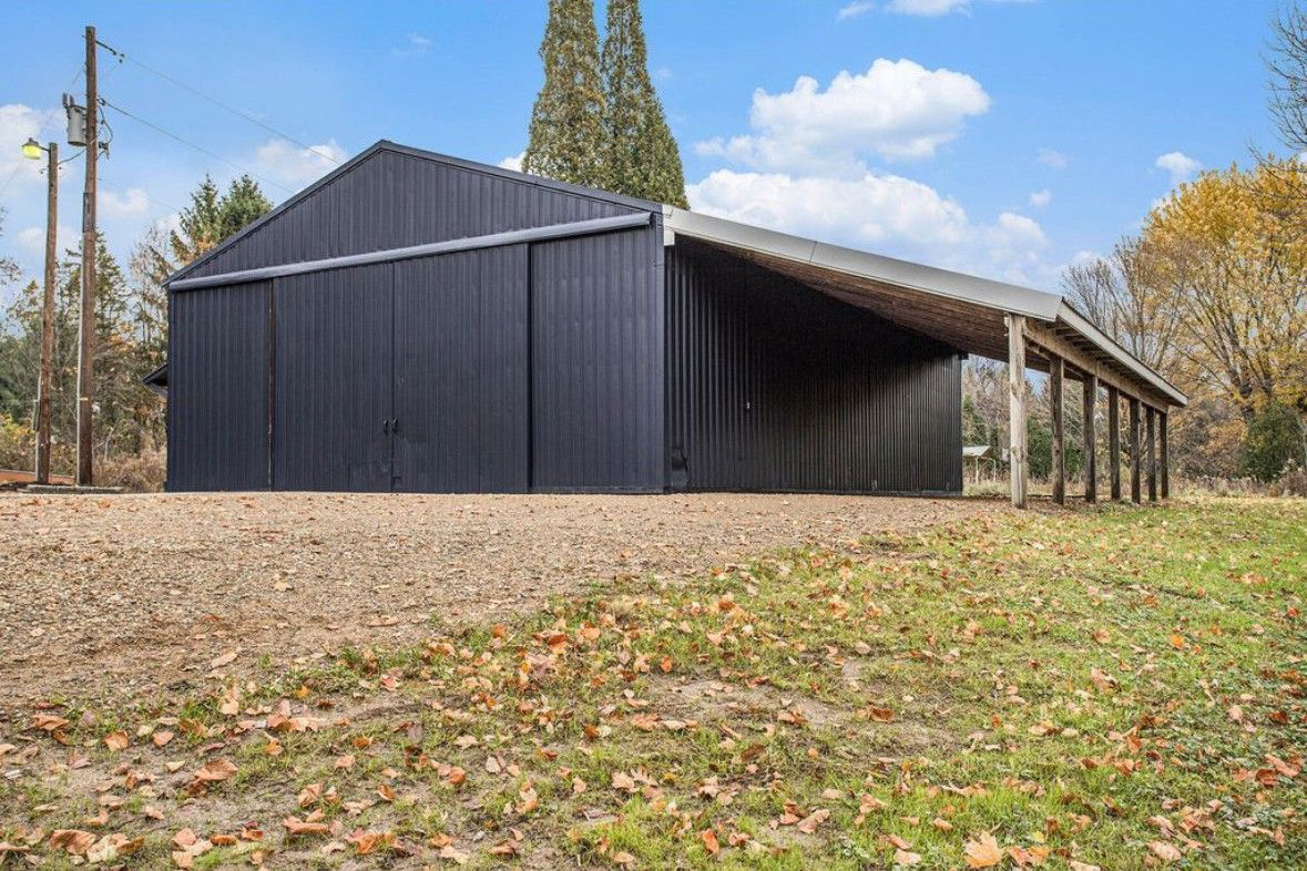 Black barn with a long covered side porch in a grassy, leaf-strewn field under a cloudy sky
