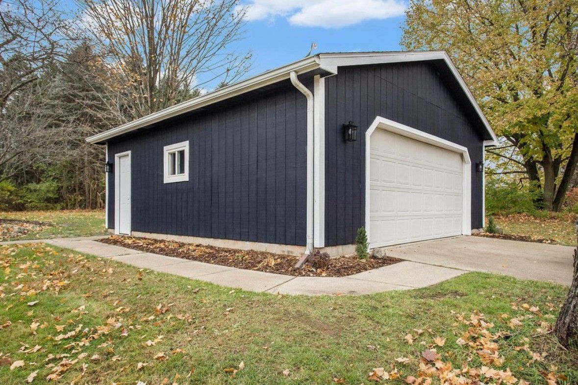 Dark blue detached garage with white trim and a white door beside a driveway and yard.