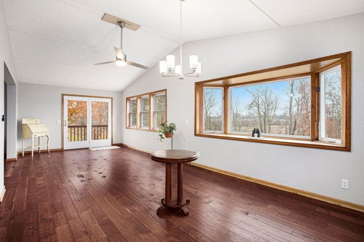 Bright empty living room with dark wood floors, white walls, chandelier, and large windows.