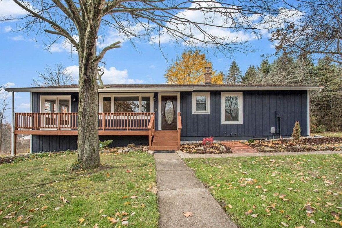 Single-story dark blue house with porch, front steps, and a large tree in the yard