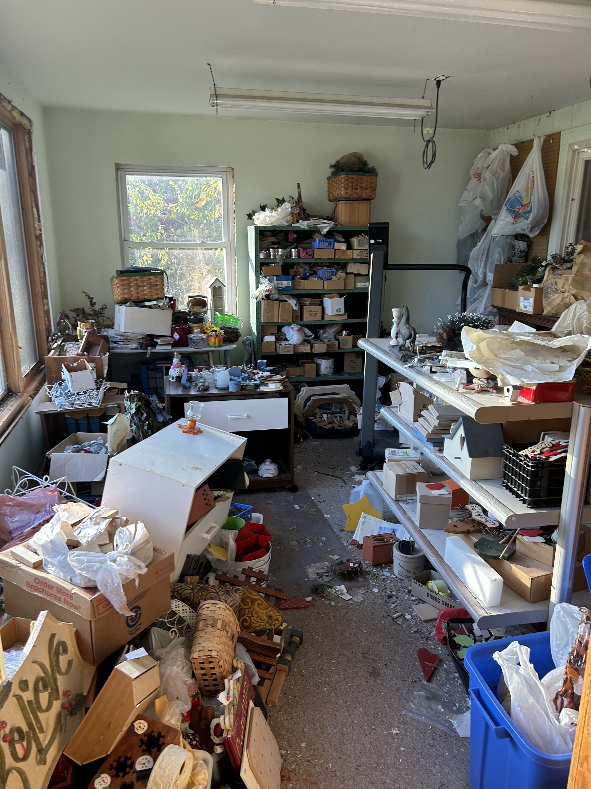 Cluttered room with shelves, boxes, and scattered papers, lit by a window at the back.