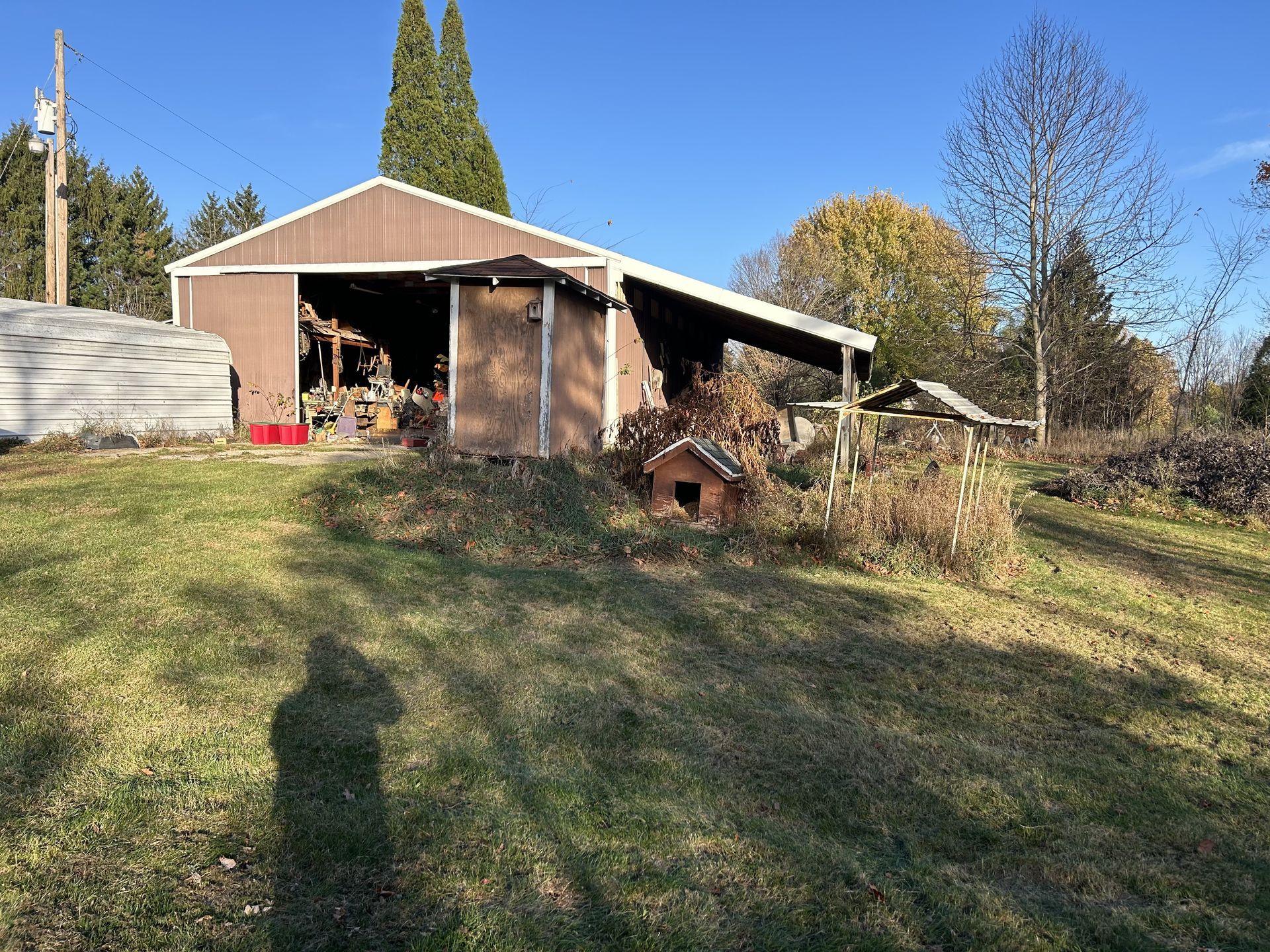 Backyard shed and small wood shelter on a grassy slope under a clear blue sky