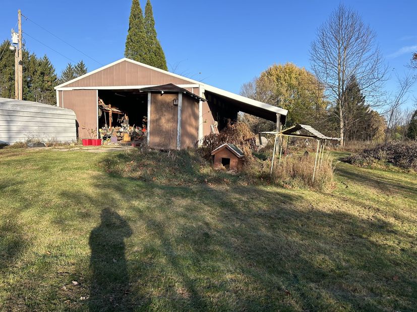 Backyard shed and small wood shelter on a grassy slope under a clear blue sky
