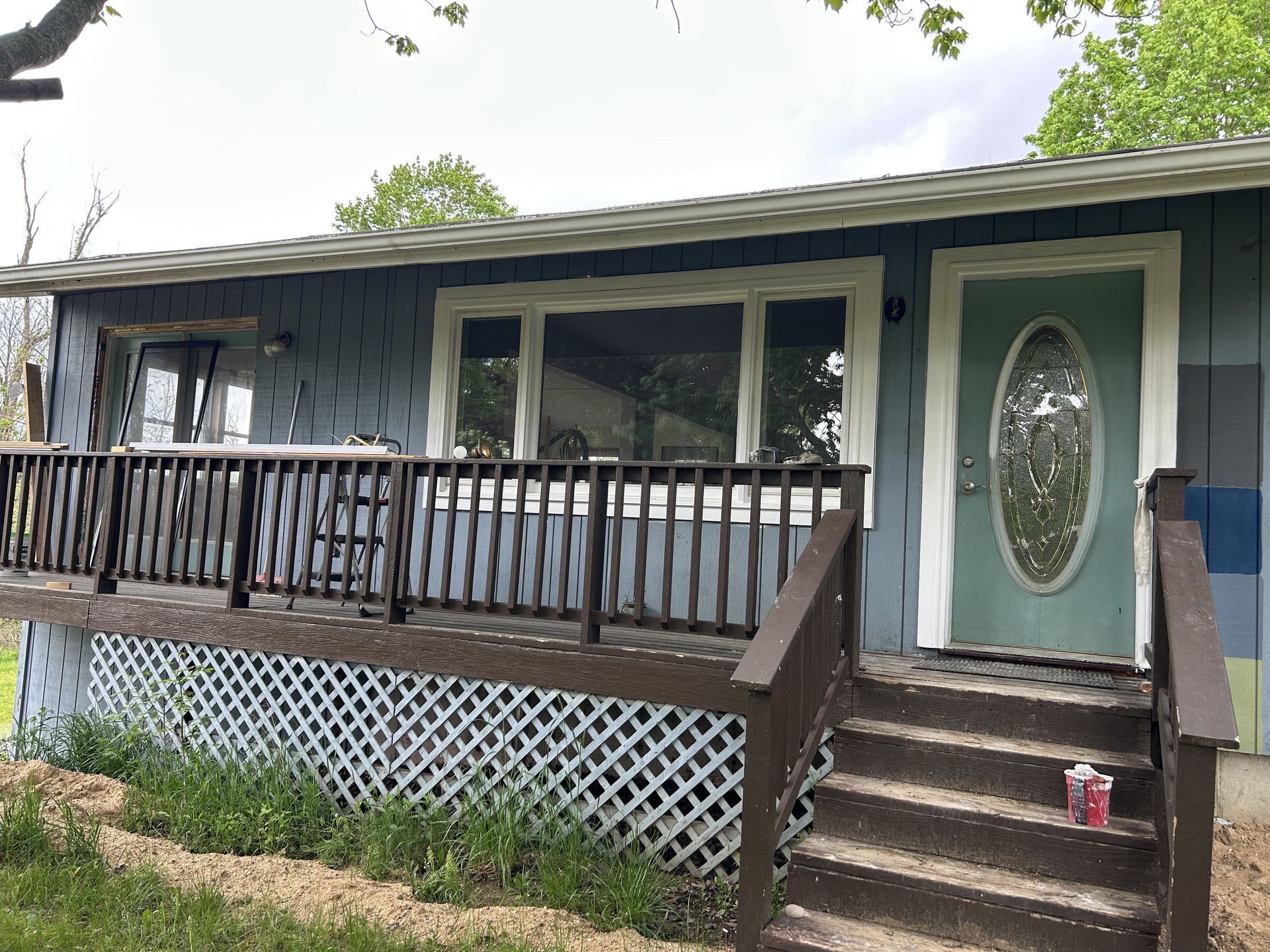 Front porch of a gray house with green trim, a wood railing, and a mint-green front door with oval glass.