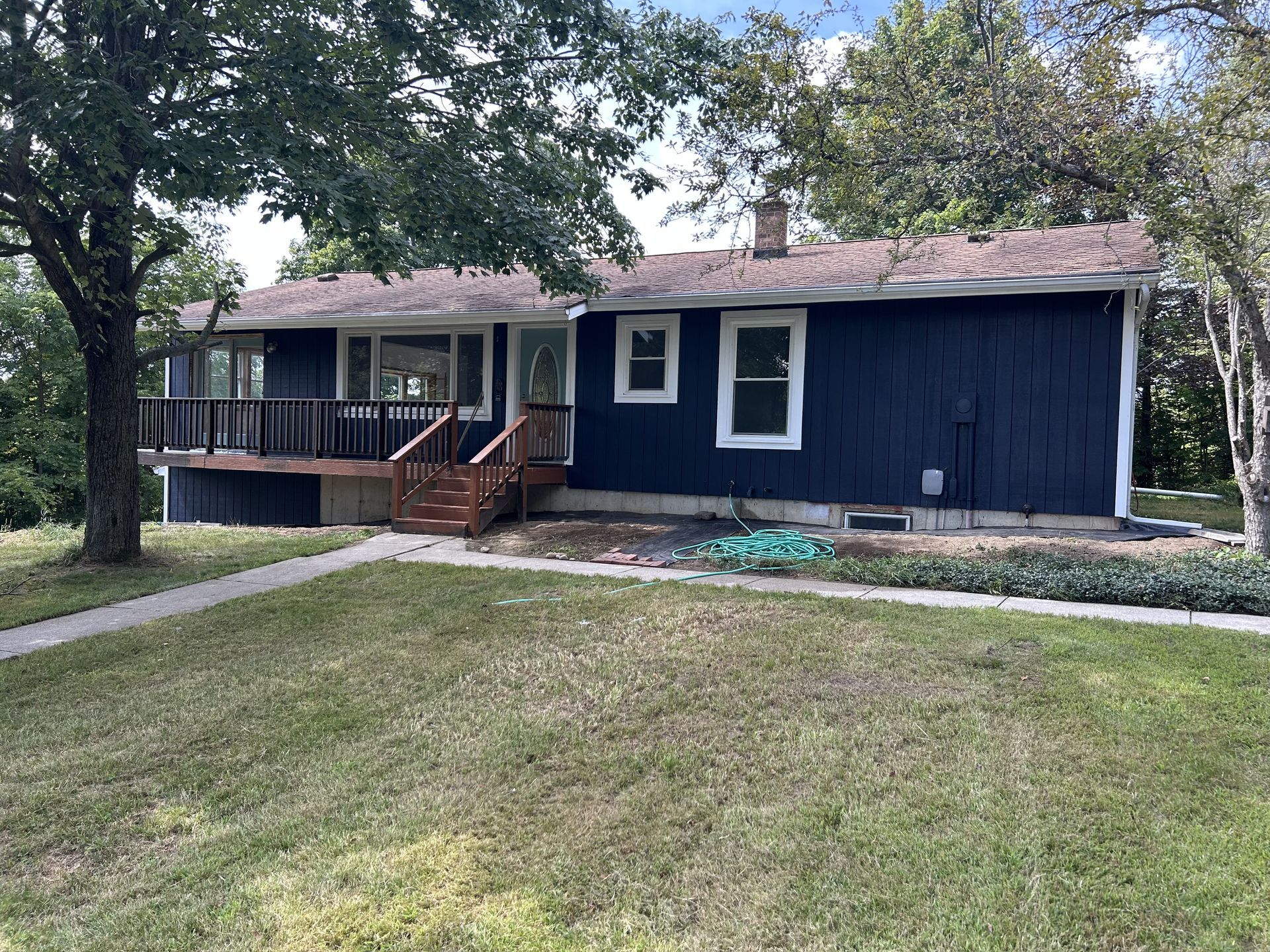 Dark blue single-story house with a front porch, steps, and a large tree in the yard.
