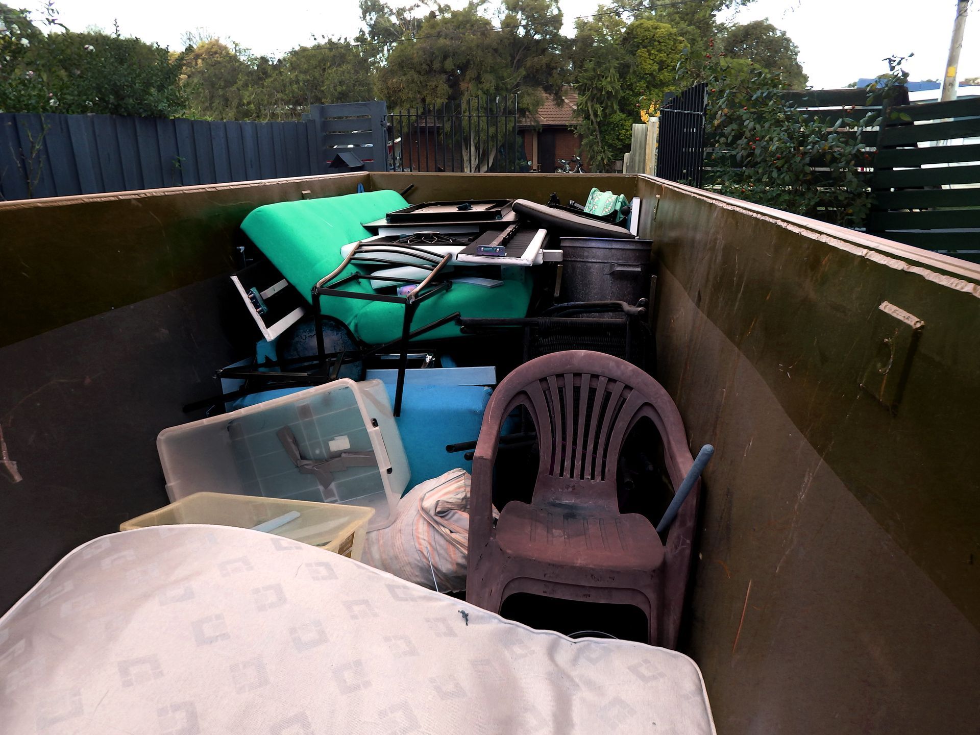 Dumpster filled with old furniture and miscellaneous items, including chairs and a table.