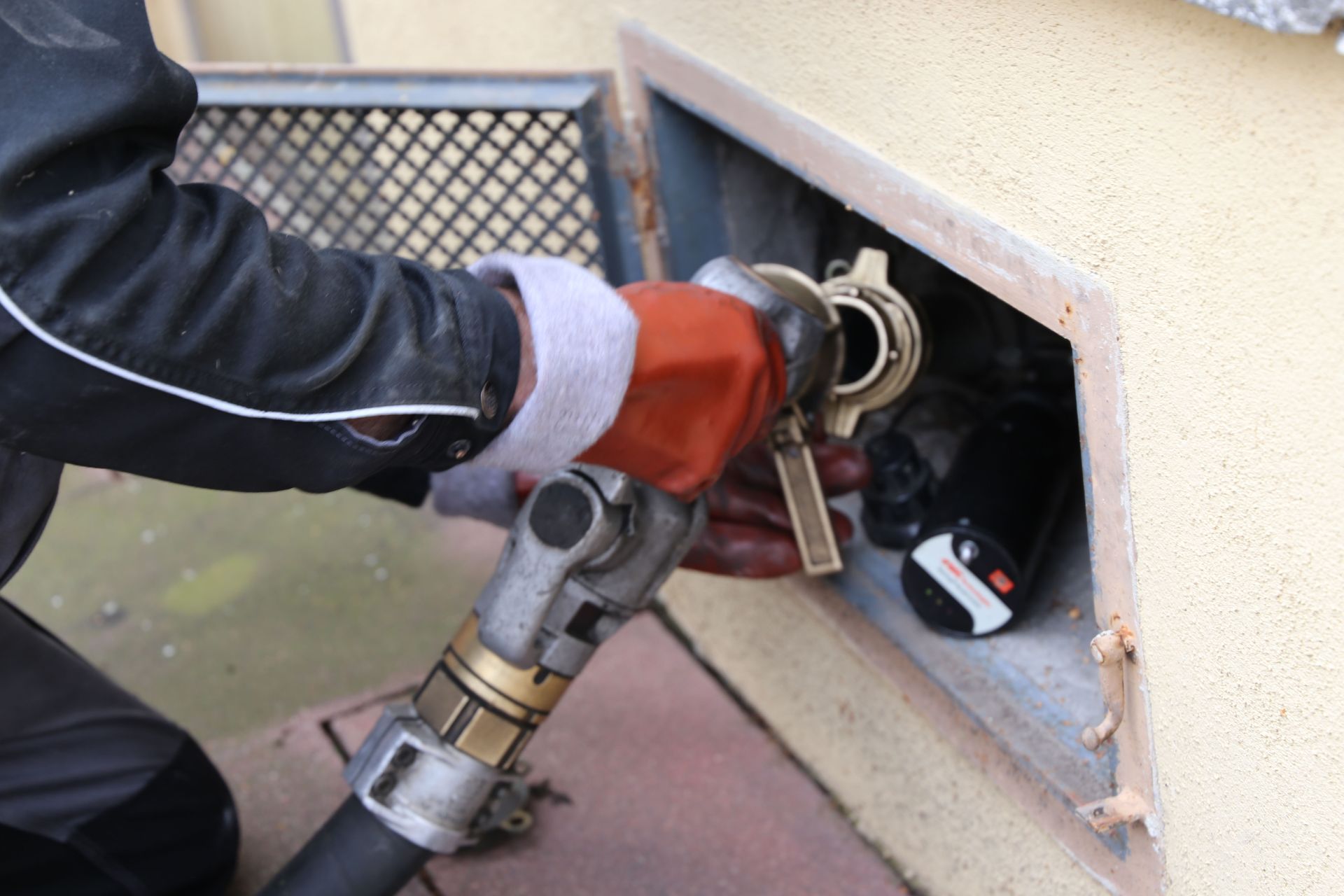 Worker connecting a hose to a wall gas inlet through an outdoor service hatch