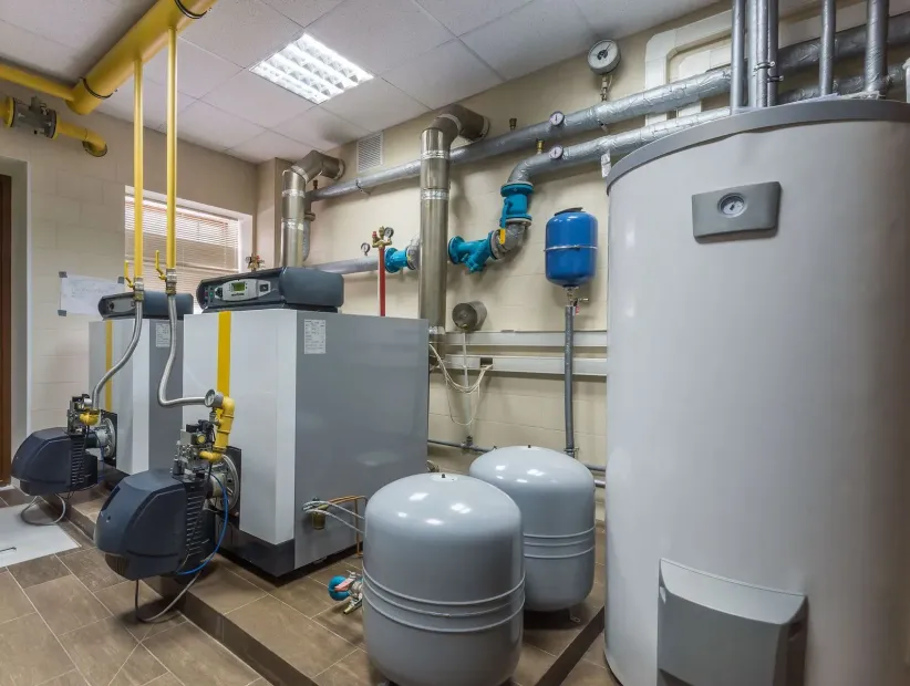 Industrial boiler room with gray tanks, pipes, and machinery in a tiled utility space