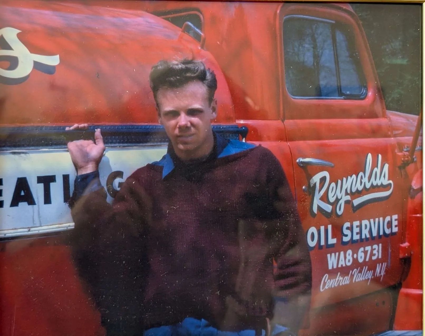 Man standing in front of a red Reynolds Oil Service truck, wearing a dark jacket, with a serious expression