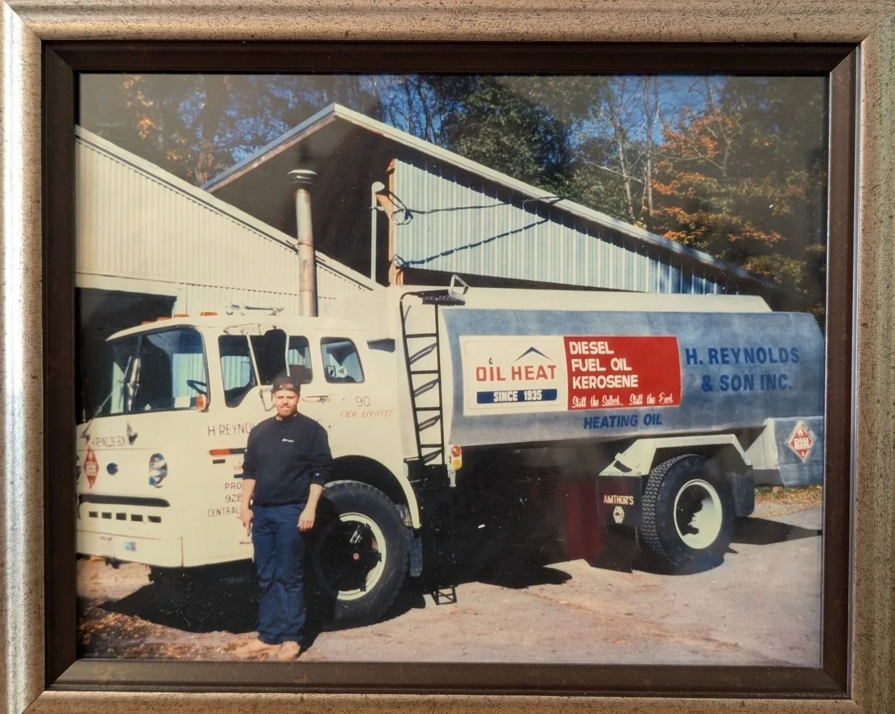 A man stands beside a white and blue oil delivery truck in front of a house.