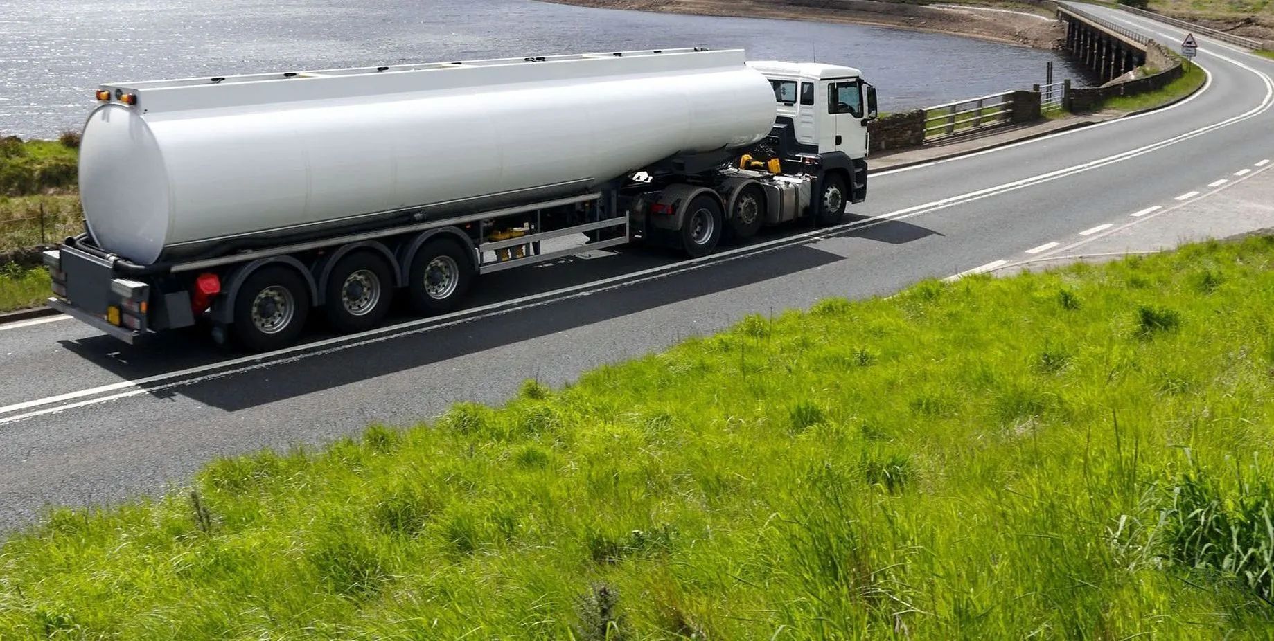 Large tanker truck driving on a highway, with a car ahead and clear blue sky.