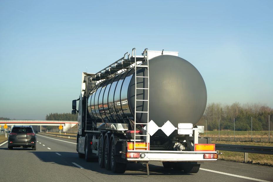 Large tanker truck driving on a highway, with a car ahead and clear blue sky.