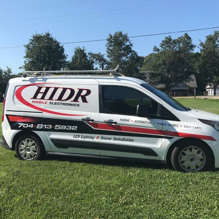 A white van with hdr written on the side is parked in a grassy field.