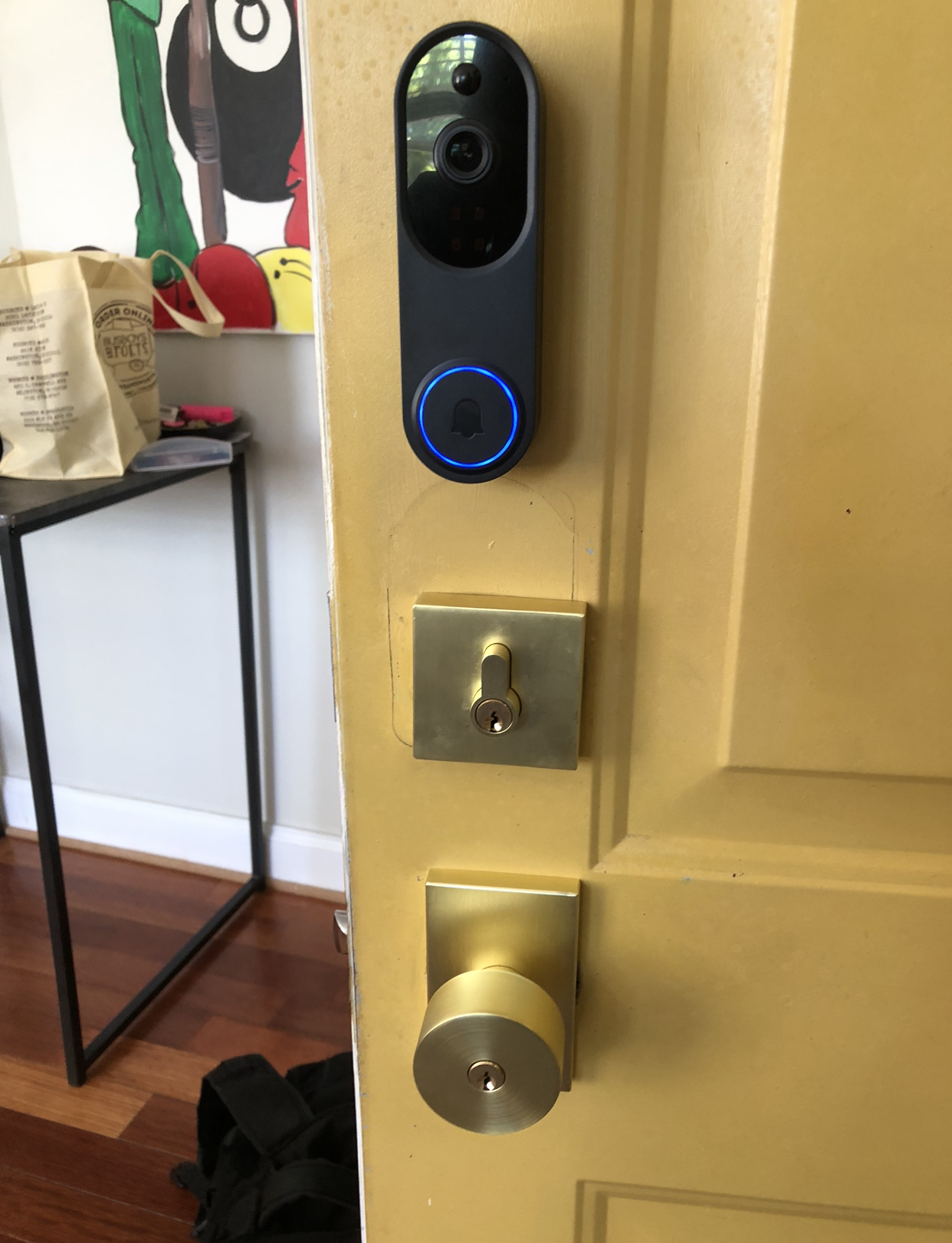Front door with a black video doorbell and blue-lit lock on a brass plate