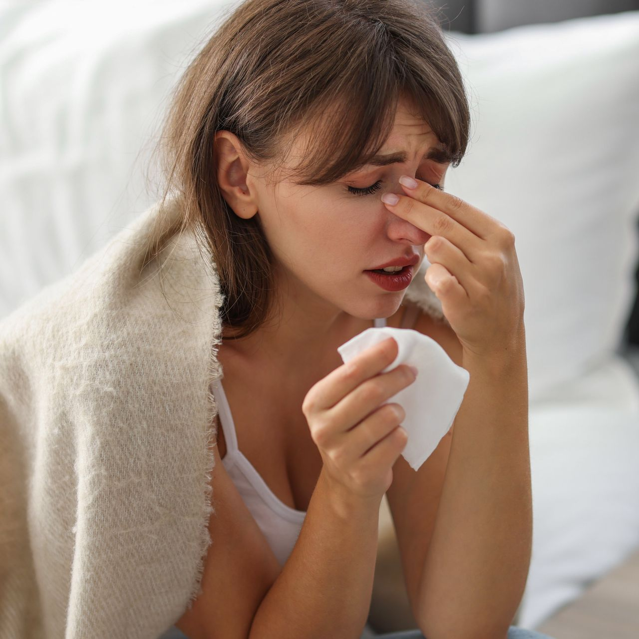 Person pinching nose, eyes closed, against a light background